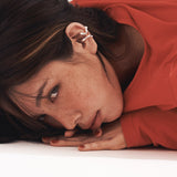 a lady with highlight hair, wearing 2 w0dd ear cuffs on one ear and laying face down on a white floor