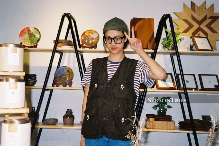Yi Hua posing a peace sign in front of a wide shelf full with her potteries