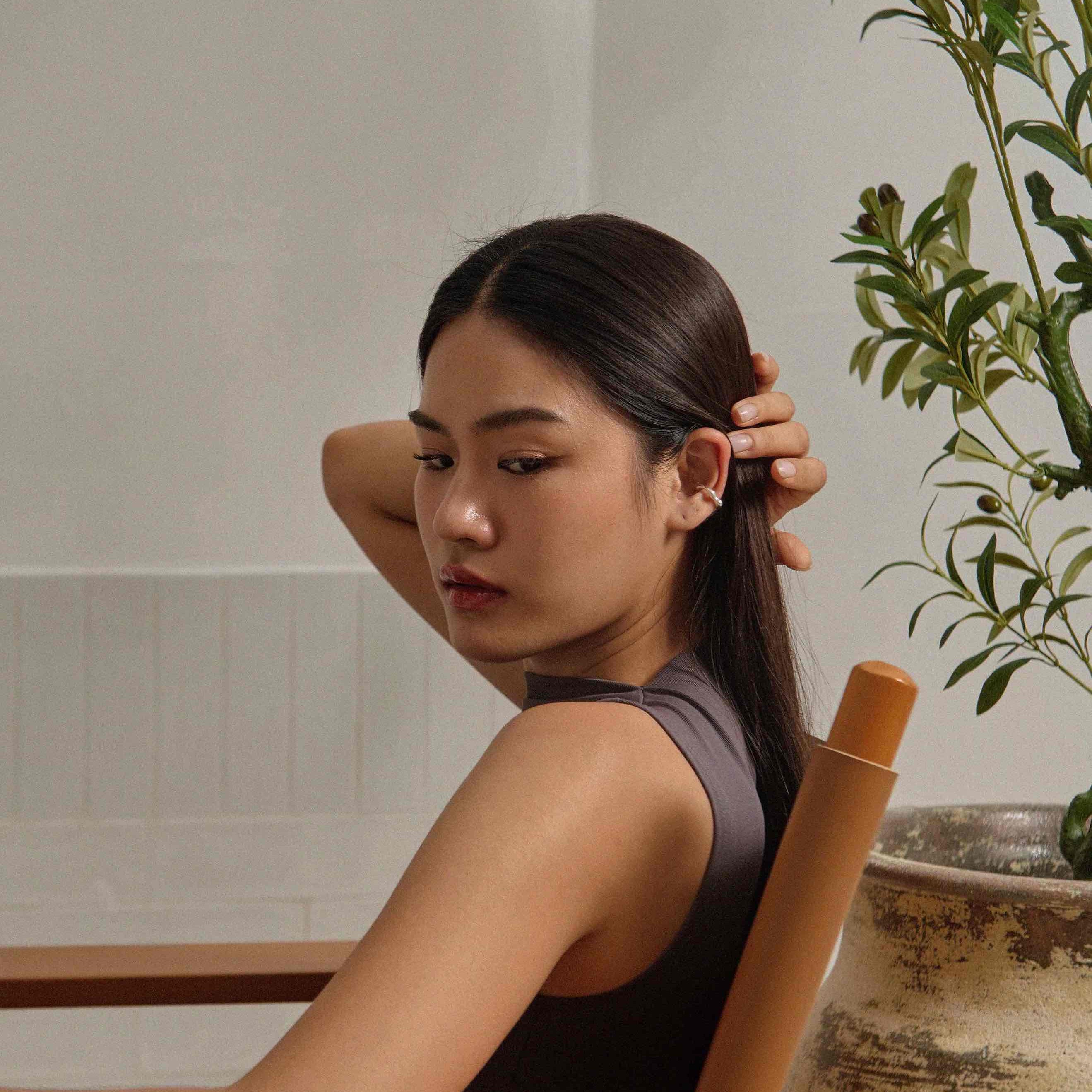lady sitting on designer's chair with w0dd's ear cuff at white wall room with a foliage plant