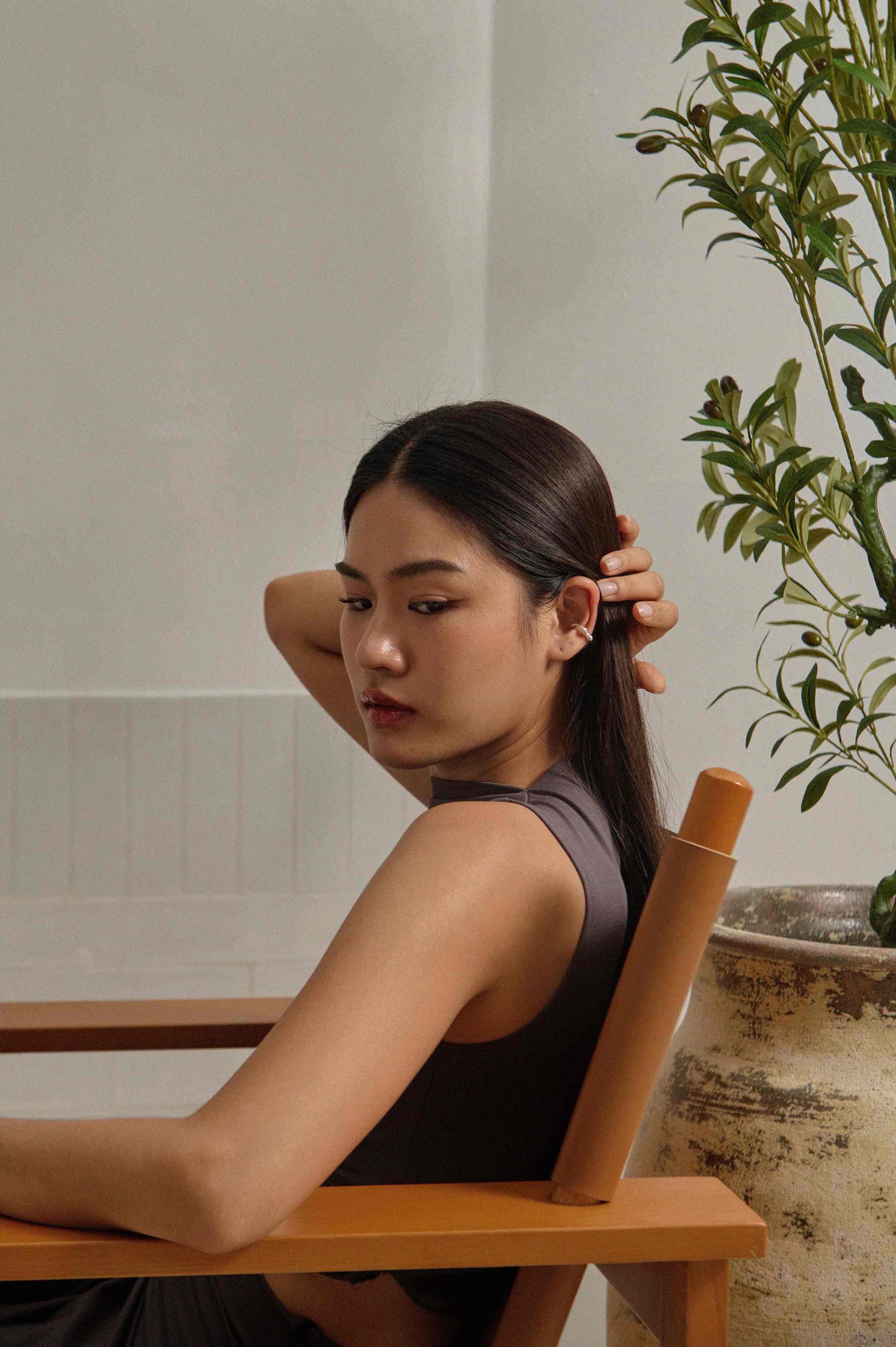 lady sitting on designer's chair with w0dd's ear cuff at white wall room with a foliage plant